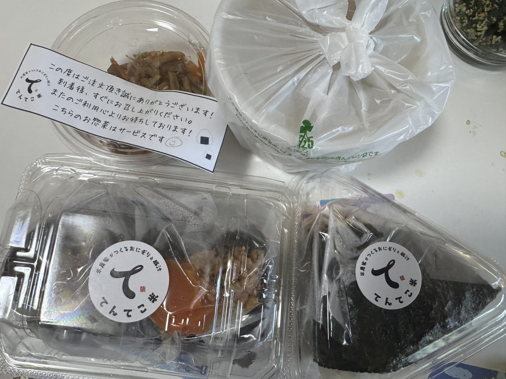 てんてこ米のパッケージに入ったおにぎりと豚汁にお惣菜と手書きメッセージが添えられた様子